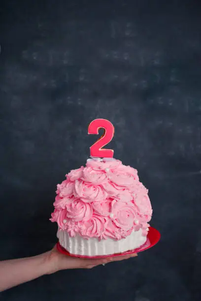 Photo of themed birthday for a fun emotional girl of the blonde smash the cake in pink color on a black background. stylized photo session tradition with sweet decor and balloons