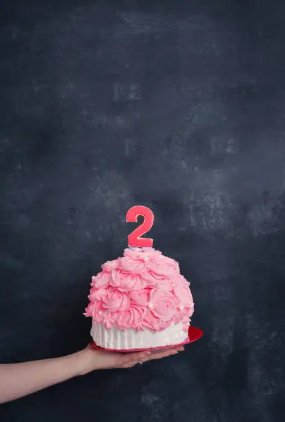 Photo of themed birthday for a fun emotional girl of the blonde smash the cake in pink color on a black background. stylized photo session tradition with sweet decor and balloons