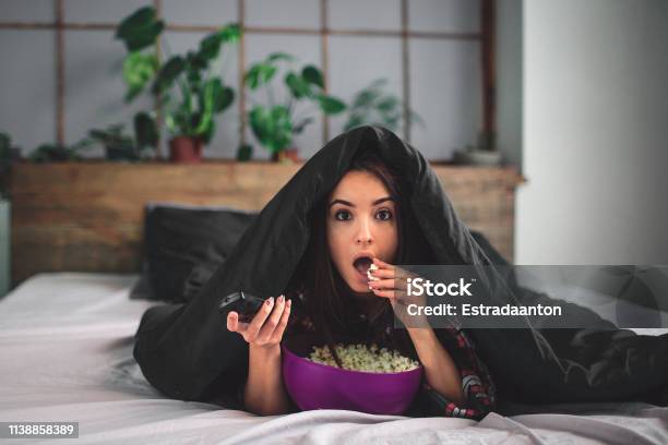 Young Woman At Home Sofa Couch In Living Room Watching Television Scary Horror Movie Or Suspense Thriller Film Or Horrible News Horrified Holding Remote Controller In Panic Eating Popcorn Bowl Stock Photo - Download Image Now