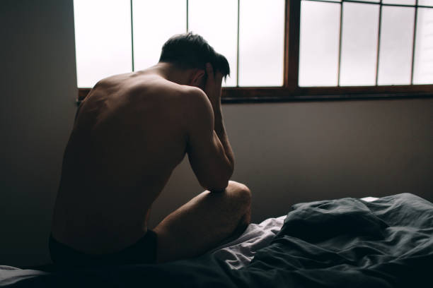 Depressed man sitting on bed in an empty room. This is major depressive disorder Depressed man sitting on bed in an empty room. This is major depressive disorder. human sexual behavior stock pictures, royalty-free photos & images