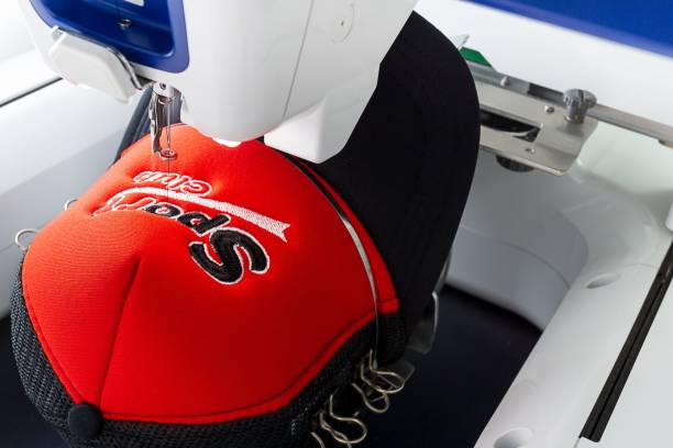 Working embroidery machine close up picture Close up image of white embroidery machine embroidering logo on red and black sport cap embroidery stock pictures, royalty-free photos & images