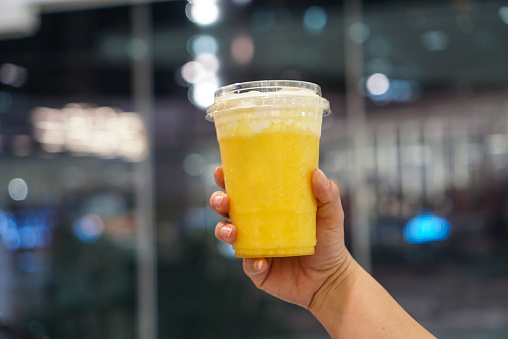 Woman holding a plastic cup of mango smoothie topped with cheese cream.