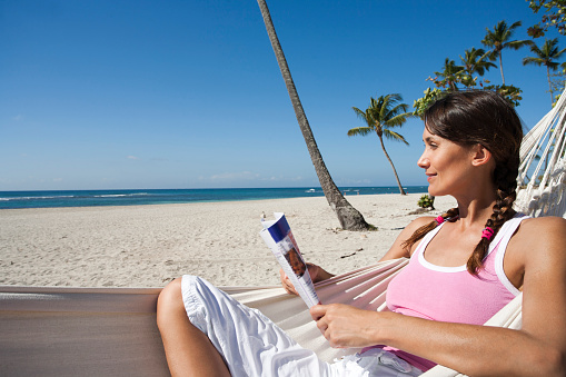 woman reading a magazine in a hammock on the beach