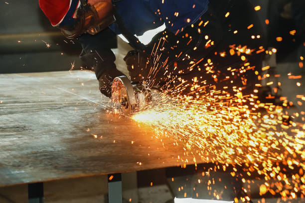 istock Worker in gloves and overalls cuts metal sheet angle grinder. Flying sparks from the disk. Industrial background with copy space. 1138879086