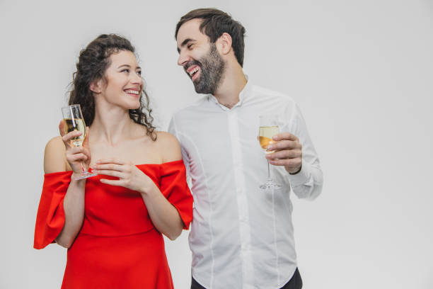 愛情の若いカップルはシャンパンを飲む。白い背景に。赤いドレスと白いシャツを着て。一緒に幸せに。 - long hair red hair women men ストックフォトと画像