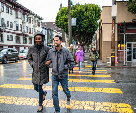 A couple followed by a larger group of pedestrians, crossing the street at a San Francisco intersection during the rain.