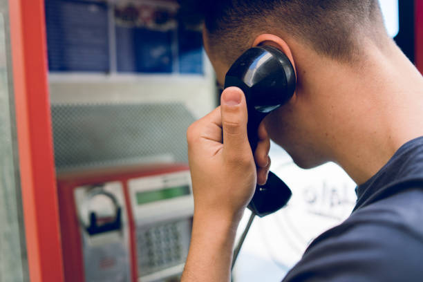 vista posteriore del giovane che effettua una chiamata dalla cabina telefonica pubblica - pay phone foto e immagini stock