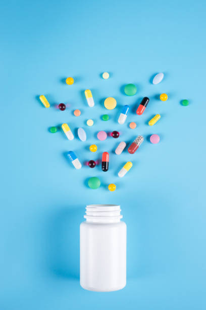 medicine green, yellow and pink pills or capsules and white bottle on a blue background with copy space. - antibiotic red medicine healthcare and medicine imagens e fotografias de stock