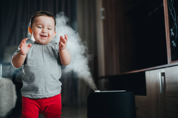 una bambina in pantaloni rossi sembra e tocca l'umidificatore. l'umidità nel concetto di casa - home interior sparse bedroom inside of foto e immagini stock