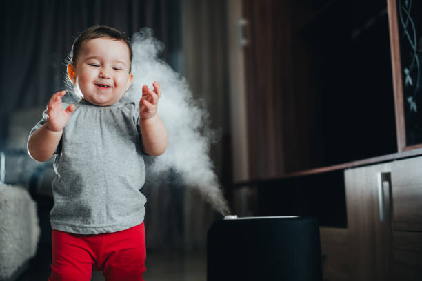 a little girl in red pants looks and touches the humidifier. moisture in the house concept - ionization imagens e fotografias de stock