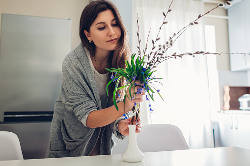 Allergy free. Happy woman putting spring flowers in vase on kitchen at home. Seasonal allergy concept.
