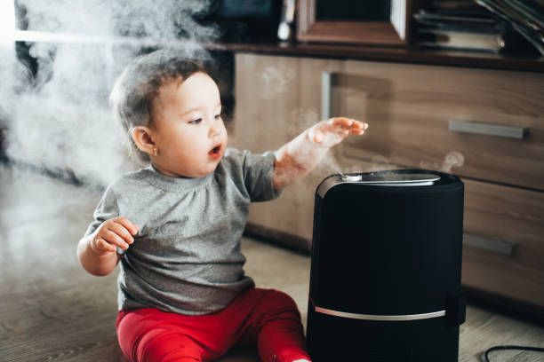 una bambina in pantaloni rossi sembra e tocca l'umidificatore. l'umidità nel concetto di casa - home interior sparse bedroom inside of foto e immagini stock