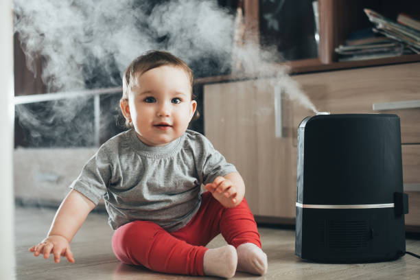 a little girl in red pants looks and touches the humidifier. moisture in the house concept - ionization imagens e fotografias de stock