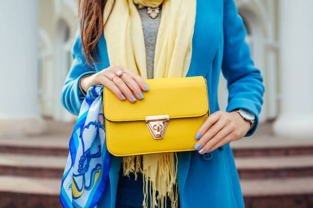 Young woman holding stylish handbag and wearing trendy blue coat. Spring female clothes and accessories. Fashion Young woman holding stylish yellow handbag and wearing trendy blue coat. Spring female clothes and accessories. Fashion spring fashion stock pictures, royalty-free photos & images