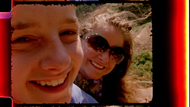 Retro style film footage of a mom and two kids smiling at camera on scenic hiking trail on family road trip.