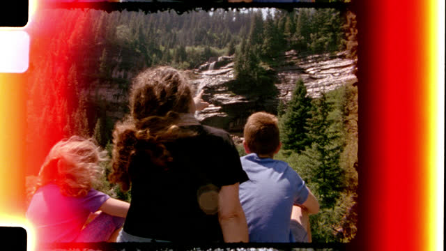 Retro style film footage of American family on cross country road trip pointing at beautiful waterfall on Bear Creek Trail.