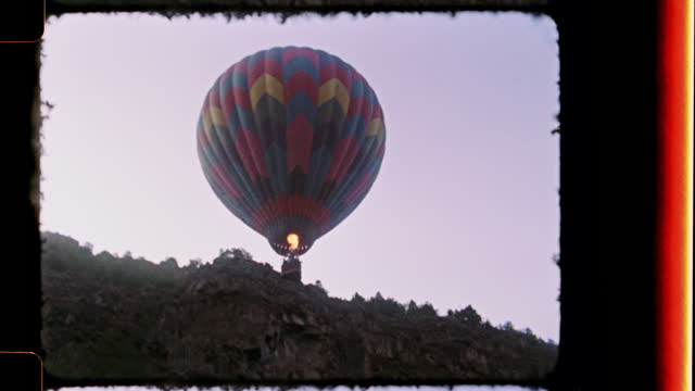 Retro style film footage of young girl in natural hot spring gazing up at hot air balloon on New Mexico camping trip.