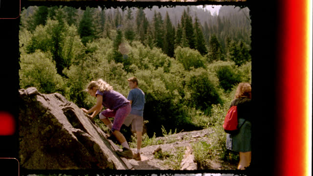 Retro style film footage of a mom and two kids on scenic hiking trail and girl climbing rocks on family camping trip to Colorado.