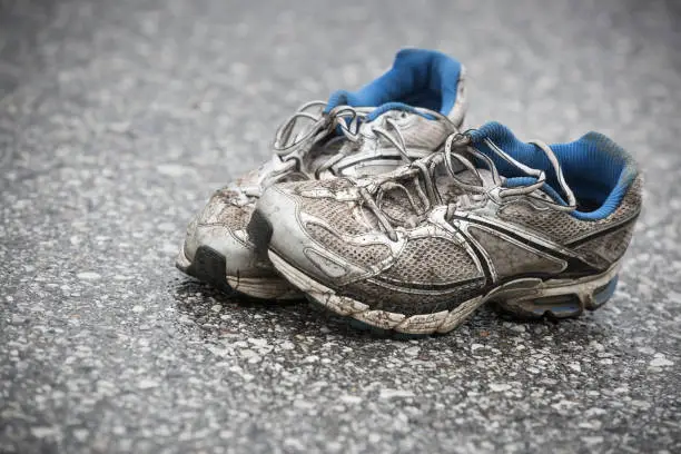 Worn, dirty, smelly and old running shoes on a tarmac road. Road running, endurance, marathon aftermath and active lifestyle concept.