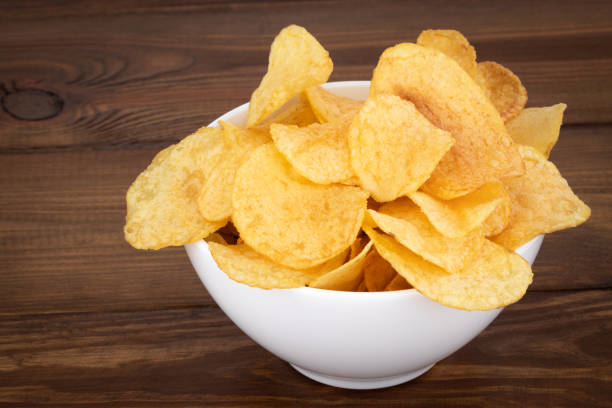 istock Crispy potato chips in bowl on wooden background 1138907575