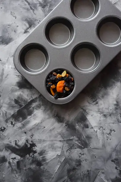 Diet and healthy eating minimalist style concept. Dried fruits in empty muffin pan on dark background top view copyspace