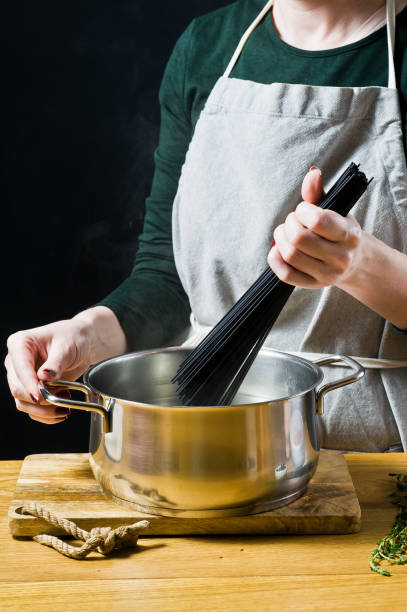 istock The chef puts black spaghetti in boiling water. Black background, side view, kitchen 1138912110