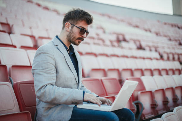 istock Young man sitting at the soccer stadium and using laptop 1138913834