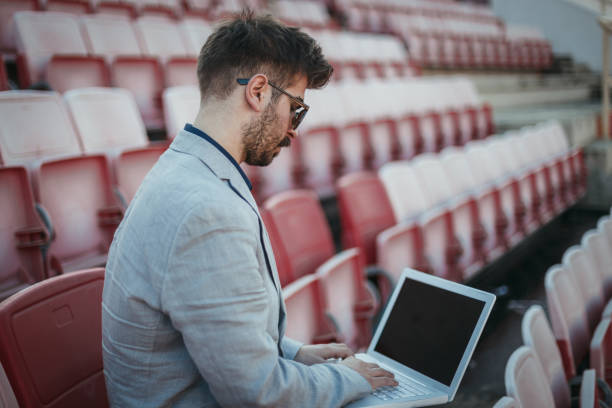 istock Young man sitting at the soccer stadium and using laptop 1138913841