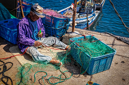 Jogashima, Kanagawa Prefect / Japan - March 20, 2019:  An unidentified fisherman repairs his nets after a morning of fishing.