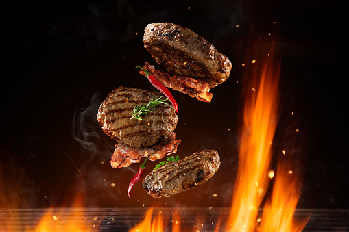 Flying beef hamburgers pieces above burning grill grid, isolated on black background. Barbecue and grill concept