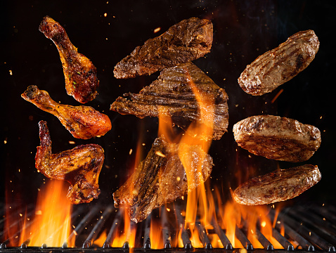Flying beef steaks, hamburgers and chicken pieces above burning grill grid, isolated on black backround. Barbecue and grill concept
