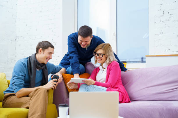 istock Friends sit on the couch, chatting and using a smartphone, desktop computer, laptop. 1138916477