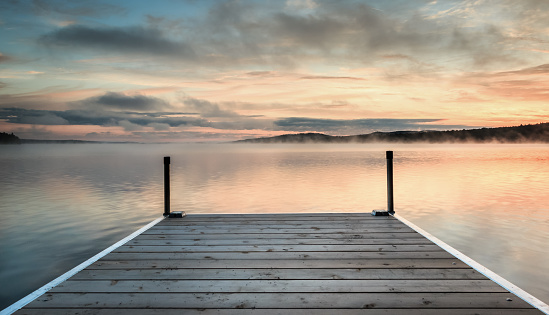 Wooden dock on a orange and blue misty lake at sunrise