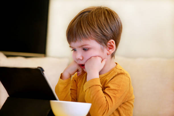 istock Child using tablet pc on bed at home. Cute boy on sofa is watching cartoon, playing games and learning from laptop. Education, fun, leisure, happiness, modern computer technology and communication. 1138919643