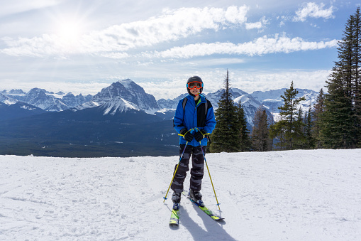 Young skier standing at the edge of a mountain range in sunny Lake Louise at the Canadian Rockies of Alberta, Canada.