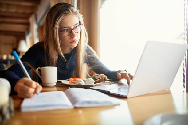 teenage girl eating breakfast and doing homework - breakfast eating people teens imagens e fotografias de stock