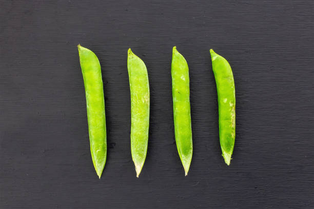 grüne, frische erbsenstange parallele gemüsesuhe auf schwarzem hintergrund kontrastierendes design-set - green pea pea pod sweet food freshness stock-fotos und bilder