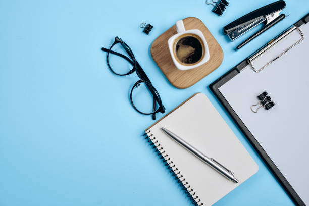 istock Office workspace with blank clip board, office supplies, pen, notepad, eyeglasses, stapler, coffee cup and spectacles on blue background. Flat lay, top view, stylish concept 1138932515