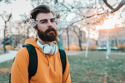 Portrait of a young bearded man with flowers in his hair on a sunny spring day