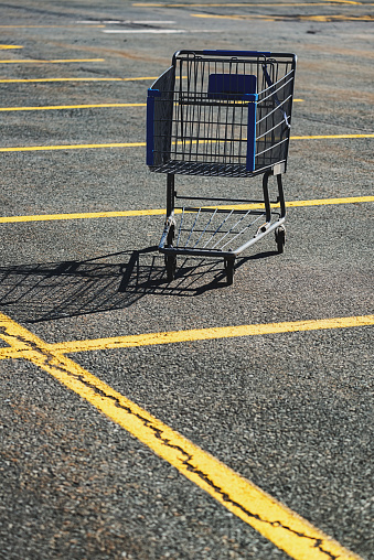 Discarded shopping cart in a large parking lot.