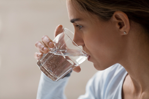 Closeup profile portrait of woman drinking pure water from glass. Beautiful young brunette female feeling thirsty, making sip of water, taking her pills, medication. Healthy lifestyle idea concept
