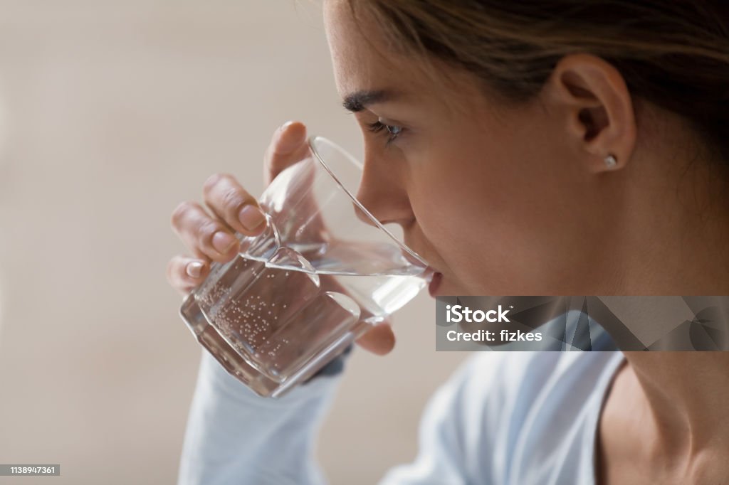 Closeup profile portrait of woman drinking pure water from glass Closeup profile portrait of woman drinking pure water from glass. Beautiful young brunette female feeling thirsty, making sip of water, taking her pills, medication. Healthy lifestyle idea concept Water Stock Photo
