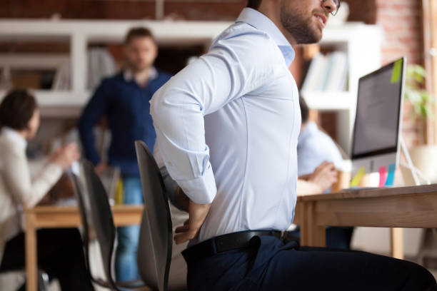 ビジネスマンは、共有オフィスに座って腰痛に苦しんでいます - low back ストックフォトと画像