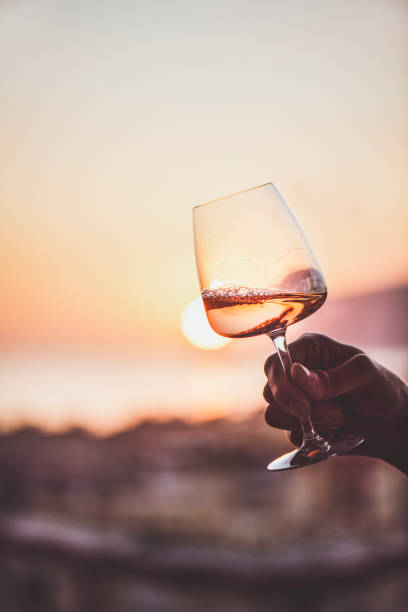 vin de rose à la main avec le coucher du soleil et la mer à l'arrière-plan - rosé photos et images de collection