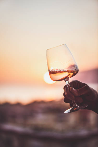 Rose wine in hand with sunset and sea at background Glass of rose wine in mans hand with sea view and sunset at background, close-up. Summer evening relaxed mood concept foxys_forest_manufacture stock pictures, royalty-free photos & images