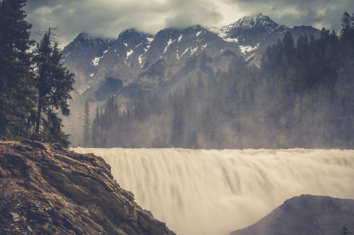 A vintage style photo of a huge rushing waterfall with giant mountains in the background.