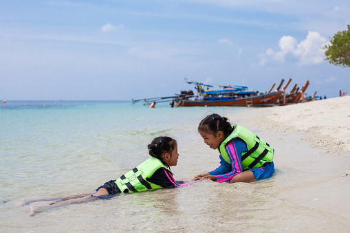 Two cute asian child girls wearing life jacket playing water in the beautiful sea together with fun in summer vacation