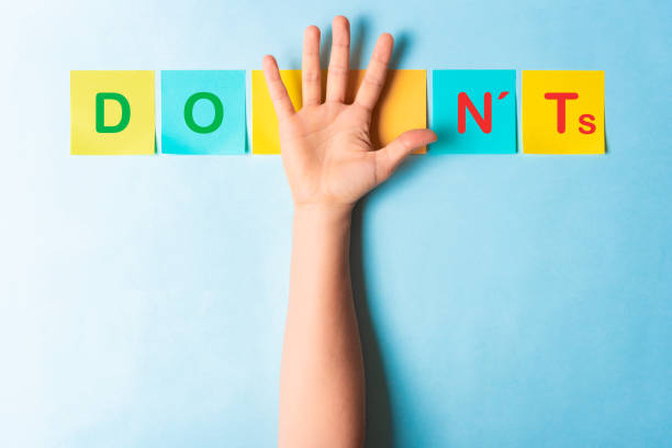 Do's and don'ts sign with multicolored sticky notes and a palm of hand showing 5 fingers on blue background stock photo