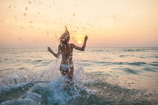 Woman running into the sea with lots of splashes at sunset