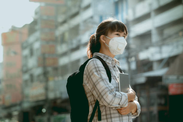 A student asian girl wearing PM 2.5 dust mask are in a city full of dust and smoke. stock photo